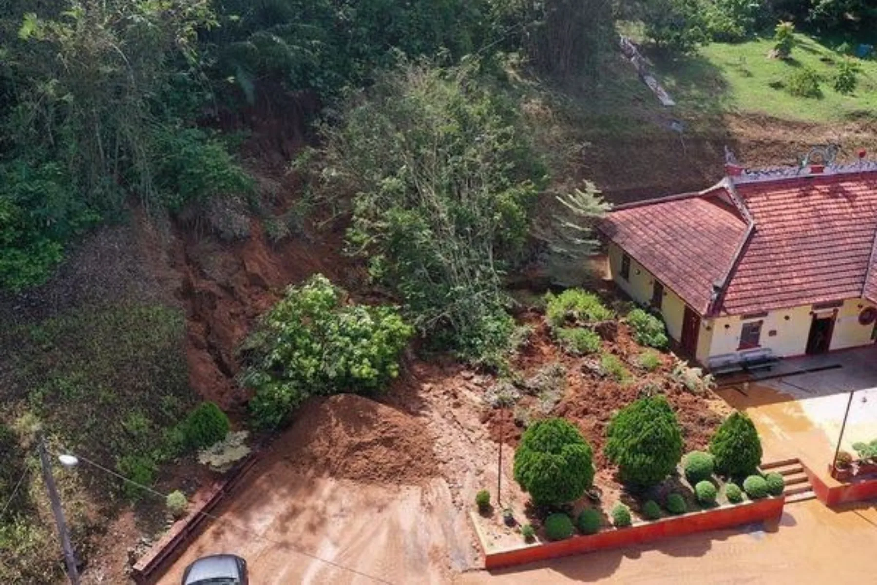 Aerial view of a landslide in Malaysia, where a slope failure has carried earth and vegetation down to the boundary wall of a building below it
