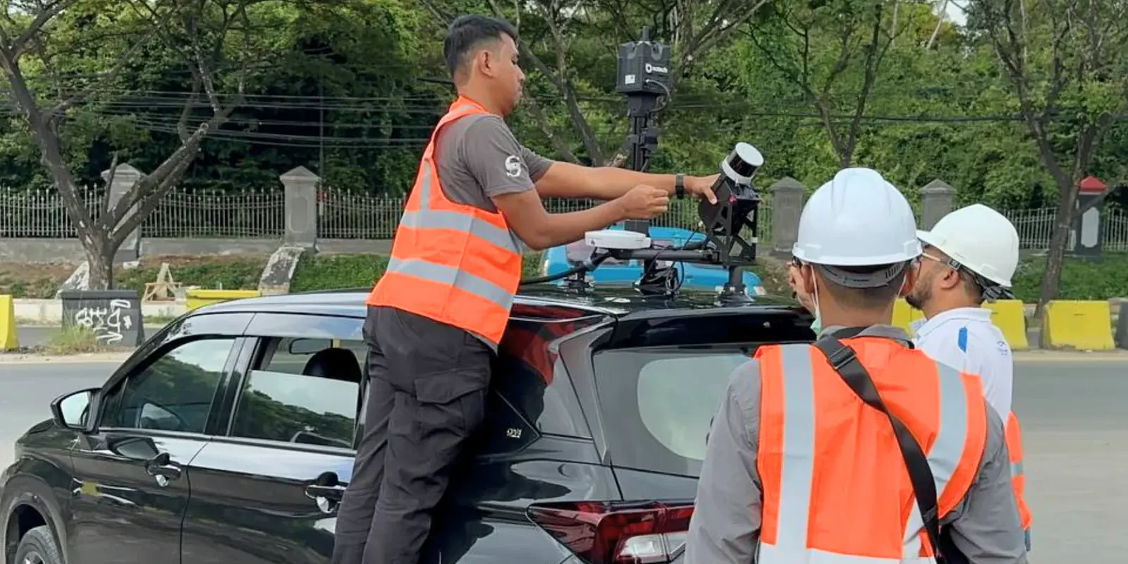 AECA crew in high-visibility vests fitting a LiDAR scanning head and GNSS antenna to the roof mount of a survey vehicle at a roadside in Malaysia