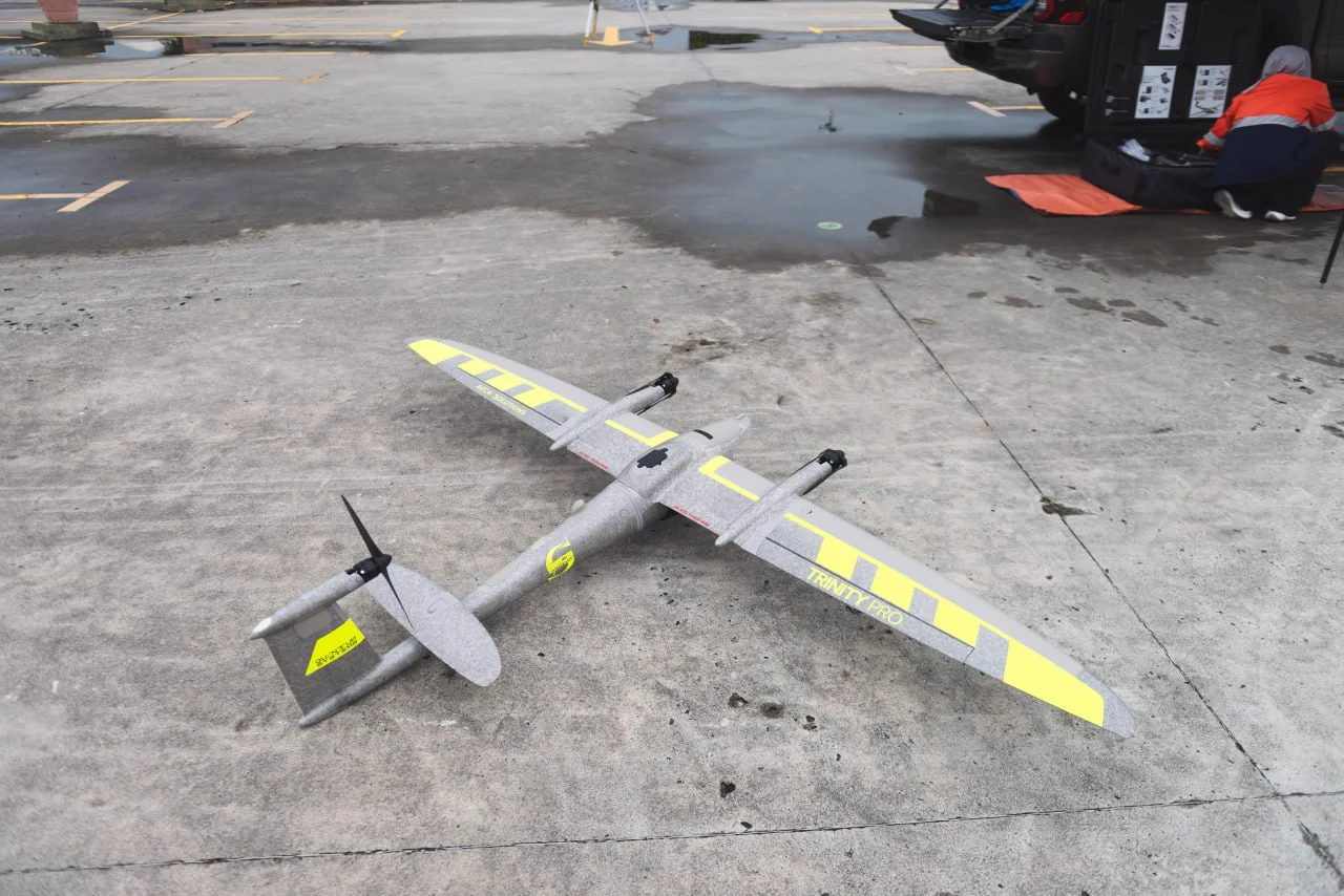 Trinity Pro fixed-wing VTOL aircraft on a hardstand with an AECA crew unpacking equipment behind it